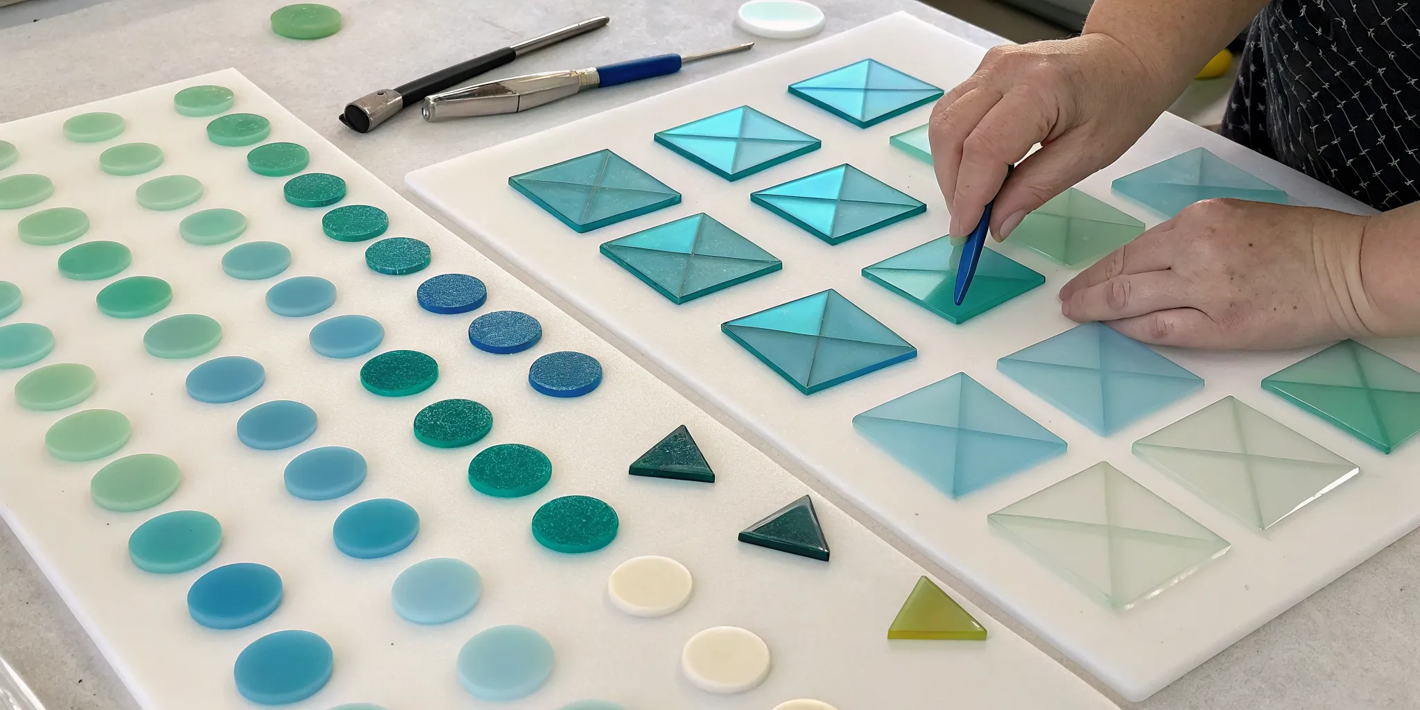 Hands arranging fusible precut glass shapes in a pattern for a fusing project.